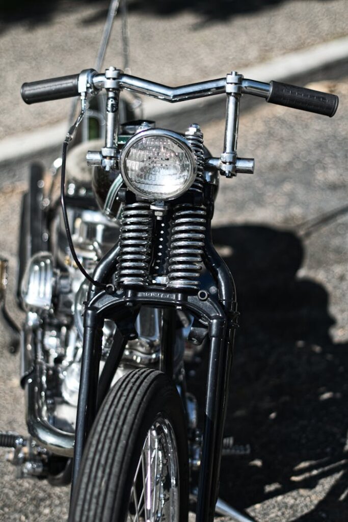 Detailed view of a classic motorcycle front handlebar and headlight outdoors in daylight.