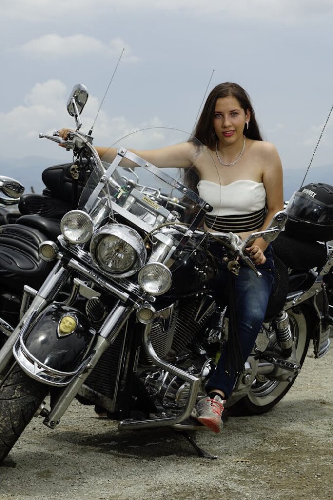 A stylish woman in denim jeans sits on a classic motorbike outdoors, showcasing adventure and freedom.